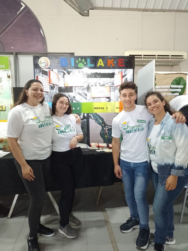 Cuatro miembros del equipo  frente a su stand en una feria de proyectos.